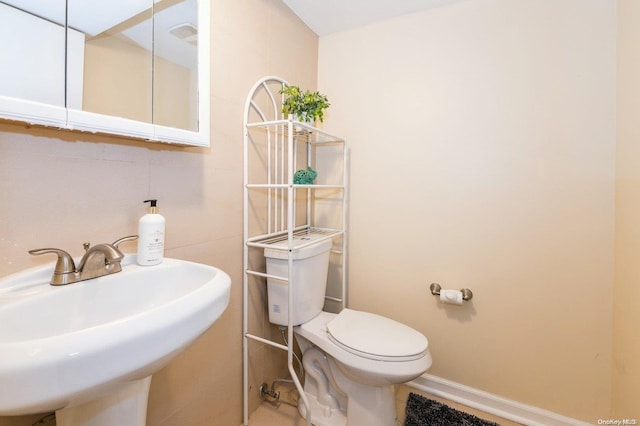 bathroom with toilet, tile walls, and sink