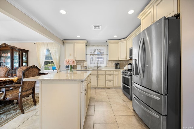 kitchen with a center island, tasteful backsplash, crown molding, cream cabinetry, and appliances with stainless steel finishes