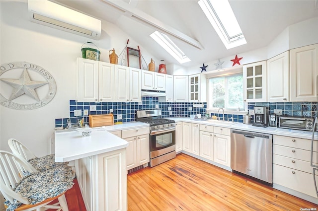 4 Landing Ln, Southampton, NY 11968 - kitchen featuring stainless steel appliances, a skylight, a wall unit AC, a sink, and lofted ceiling