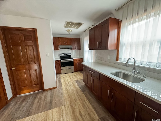 kitchen featuring light stone countertops, tasteful backsplash, light hardwood / wood-style floors, sink, and stainless steel stove