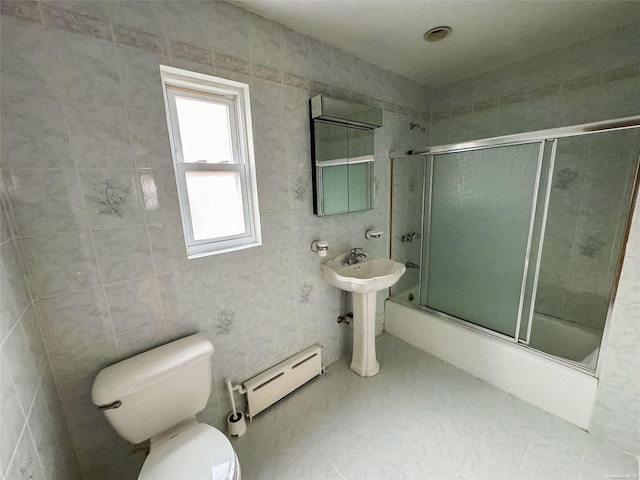 full bathroom featuring sink, a baseboard heating unit, toilet, shower / bath combination with glass door, and tile walls