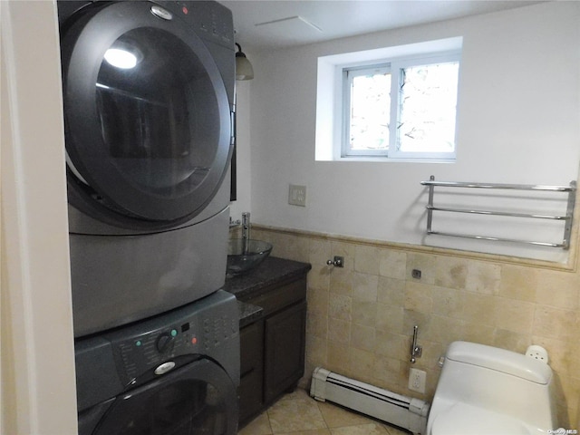 laundry area with baseboard heating, stacked washer and dryer, light tile patterned floors, and tile walls