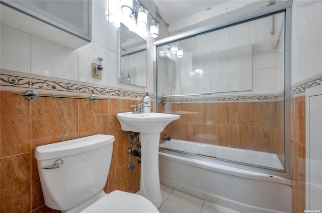 bathroom featuring tile patterned flooring, toilet, bath / shower combo with glass door, and tile walls