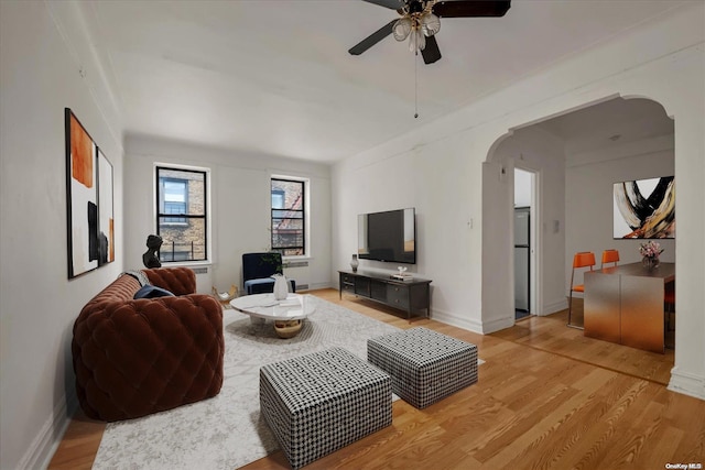 living room featuring ceiling fan, arched walkways, light wood-style floors, and baseboards