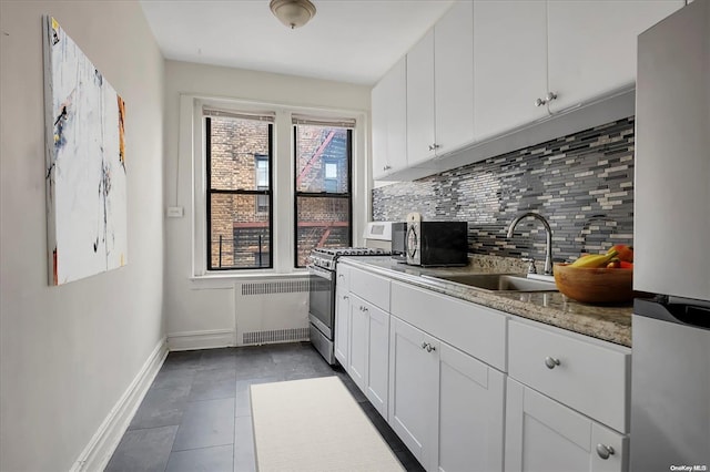 kitchen featuring radiator, white cabinets, appliances with stainless steel finishes, a sink, and decorative backsplash