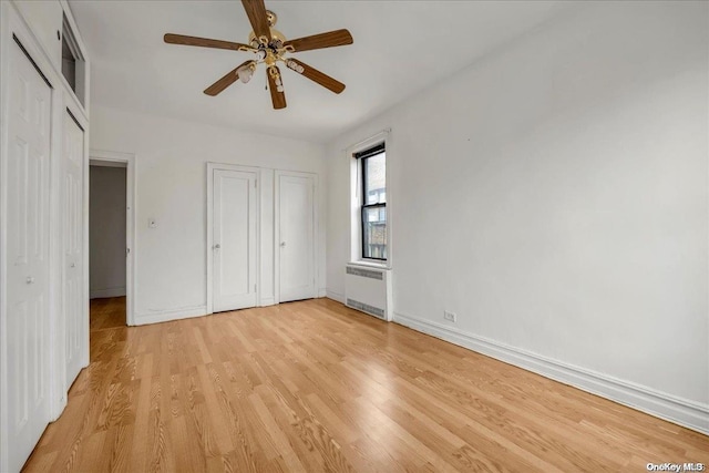 unfurnished bedroom featuring radiator heating unit, light wood finished floors, ceiling fan, and baseboards