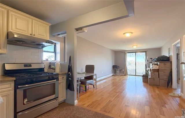 kitchen with a baseboard heating unit, light hardwood / wood-style flooring, stainless steel gas stove, decorative backsplash, and cream cabinetry