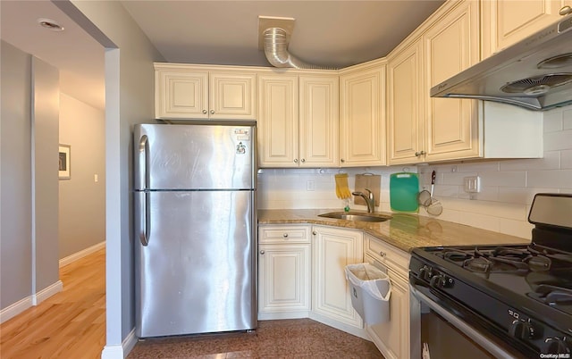 kitchen with light stone countertops, tasteful backsplash, sink, black gas range, and stainless steel refrigerator