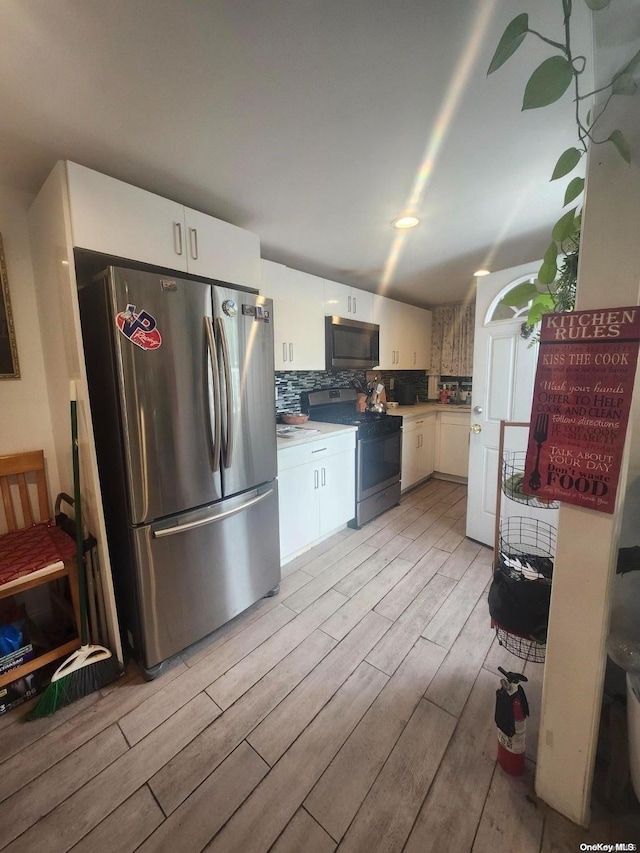 kitchen with backsplash, white cabinets, stainless steel appliances, and light hardwood / wood-style floors