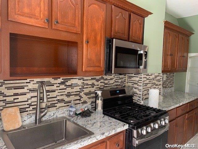 kitchen with decorative backsplash, stainless steel appliances, light stone countertops, and sink