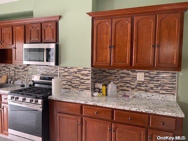 kitchen with backsplash, light stone counters, and appliances with stainless steel finishes