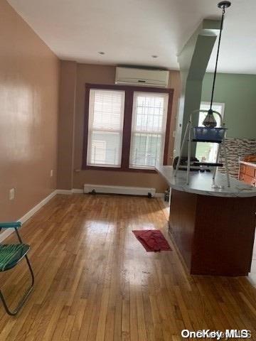 home office featuring wood-type flooring, a wall unit AC, and a baseboard heating unit