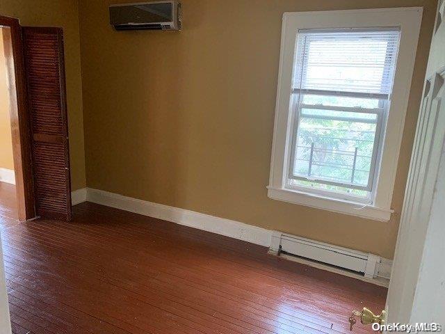 unfurnished room featuring baseboard heating, a wall mounted AC, and dark wood-type flooring