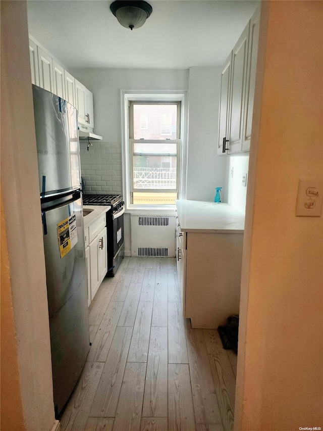 kitchen with gas range, white cabinetry, radiator heating unit, stainless steel fridge, and light hardwood / wood-style floors