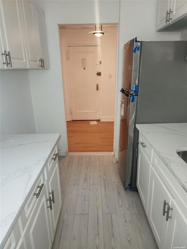 kitchen featuring light stone countertops, light wood-type flooring, white cabinetry, and stainless steel refrigerator