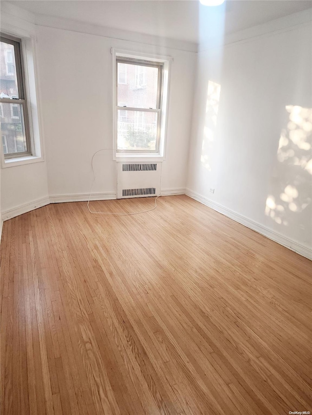 unfurnished room featuring light wood-type flooring, radiator heating unit, and crown molding