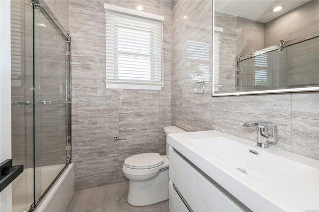 full bathroom with vanity, toilet, tile walls, and combined bath / shower with glass door