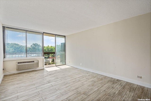 spare room with a textured ceiling, a wall mounted air conditioner, and light wood-type flooring