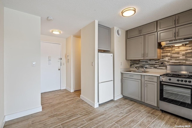 kitchen featuring stainless steel gas range oven, sink, light hardwood / wood-style flooring, a textured ceiling, and white fridge