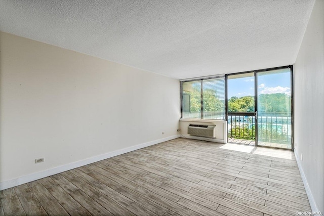 spare room with a textured ceiling, light wood-type flooring, and a wall unit AC