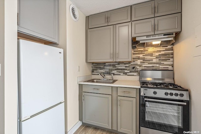 kitchen with sink, stainless steel gas range oven, white refrigerator, backsplash, and a textured ceiling