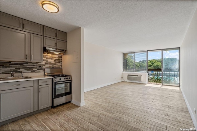 kitchen featuring decorative backsplash, a textured ceiling, gas stove, sink, and light hardwood / wood-style flooring