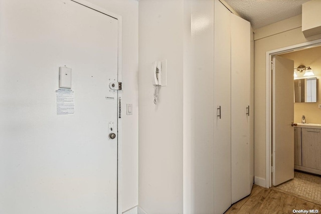 hallway with sink, a textured ceiling, and light wood-type flooring