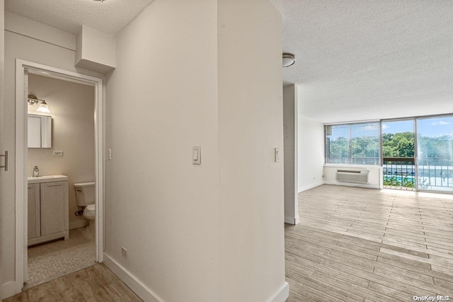 hallway featuring a wall mounted air conditioner, a textured ceiling, sink, a wall of windows, and light hardwood / wood-style floors