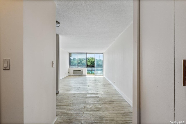 corridor with a textured ceiling, light hardwood / wood-style floors, and a wall mounted AC