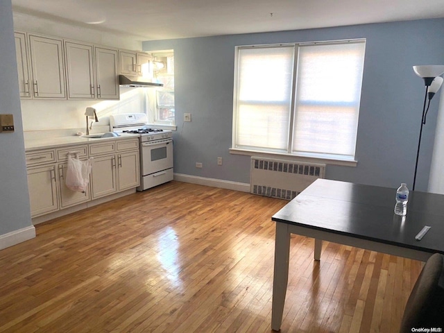 kitchen featuring light wood-type flooring, radiator, white gas stove, and sink