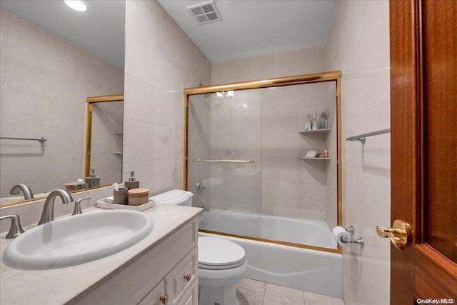 bathroom featuring toilet, visible vents, vanity, tile walls, and tile patterned floors