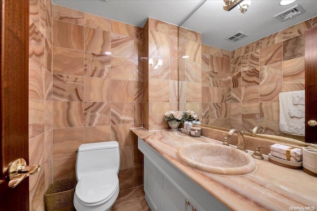 bathroom featuring visible vents, toilet, vanity, and tile walls