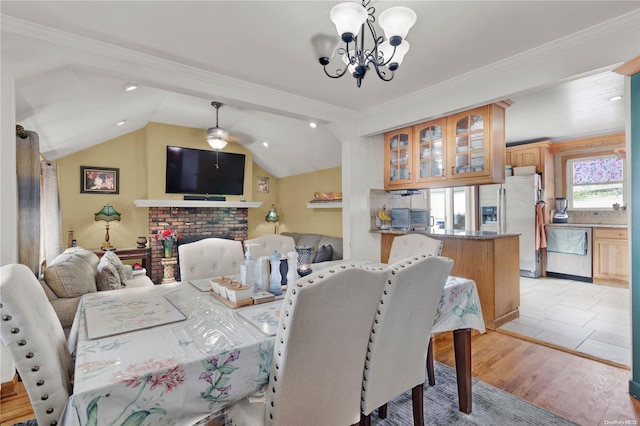 dining area featuring a notable chandelier, crown molding, light hardwood / wood-style floors, vaulted ceiling, and a fireplace