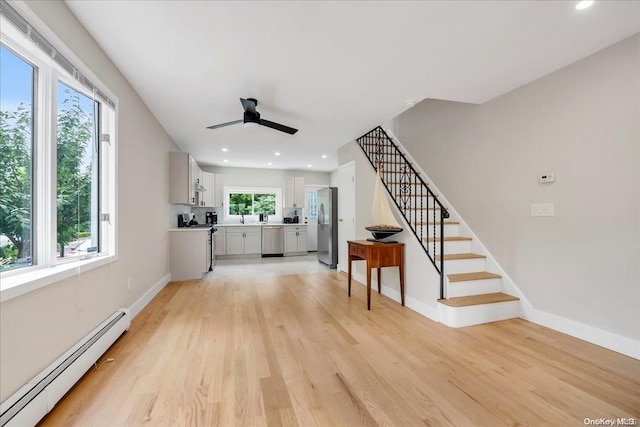 unfurnished living room with ceiling fan, sink, light wood-type flooring, and a baseboard heating unit