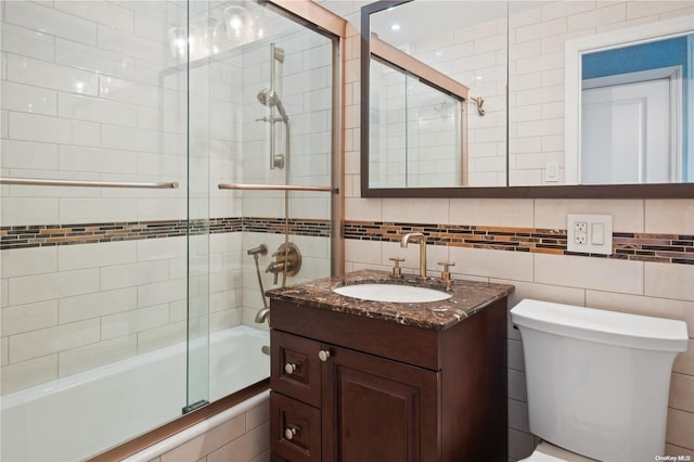 full bathroom featuring vanity, backsplash, bath / shower combo with glass door, toilet, and tile walls