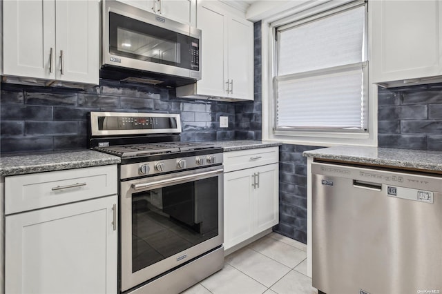 kitchen with decorative backsplash, dark stone counters, stainless steel appliances, white cabinets, and light tile patterned flooring