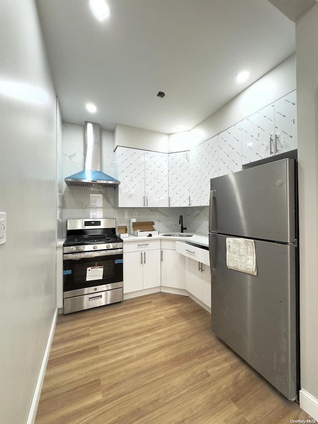 kitchen with white cabinetry, sink, wall chimney exhaust hood, appliances with stainless steel finishes, and light wood-type flooring