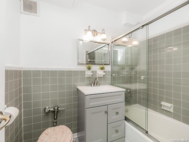 bathroom featuring vanity, bath / shower combo with glass door, and tile walls