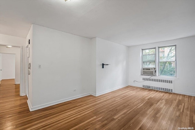 spare room with radiator heating unit, cooling unit, and wood-type flooring