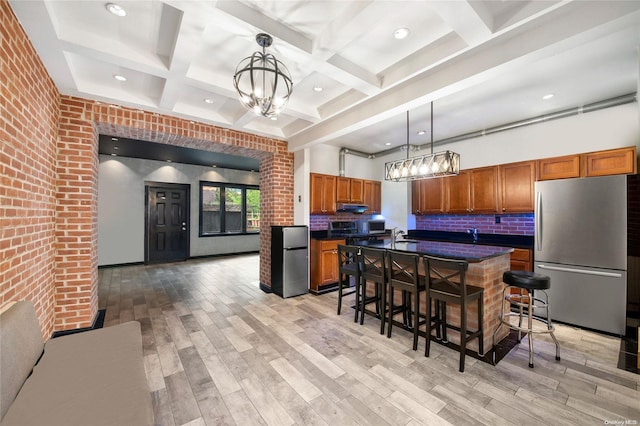 kitchen with appliances with stainless steel finishes, beamed ceiling, decorative light fixtures, light hardwood / wood-style floors, and brick wall