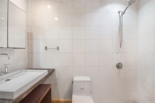 bathroom with tiled shower, vanity, tile walls, and toilet