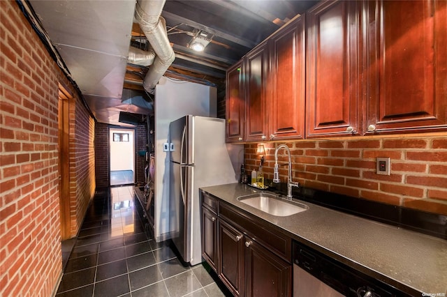 kitchen featuring dark tile patterned floors, sink, brick wall, and stainless steel appliances