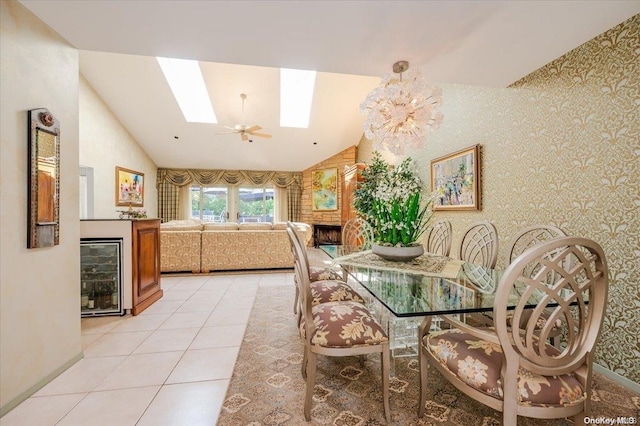 tiled dining space featuring lofted ceiling with skylight, a fireplace, beverage cooler, and ceiling fan with notable chandelier