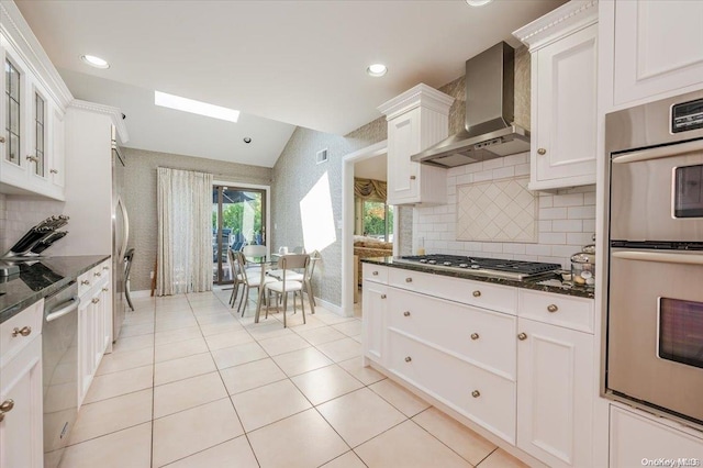 kitchen featuring white cabinets, stainless steel appliances, dark stone counters, and wall chimney range hood