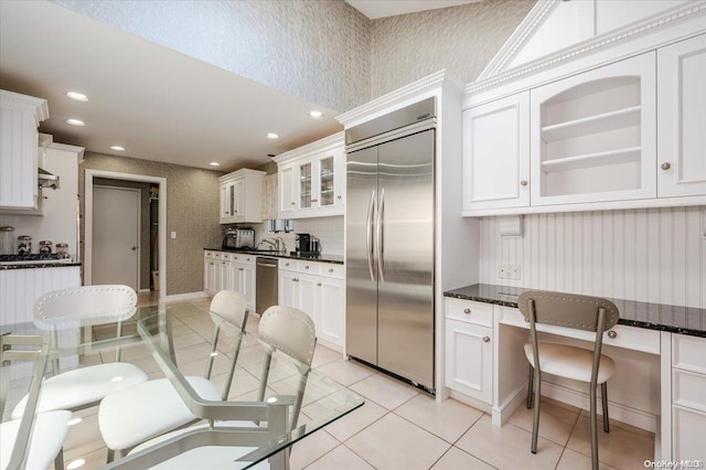 kitchen featuring light tile patterned flooring, built in desk, white cabinets, and stainless steel appliances