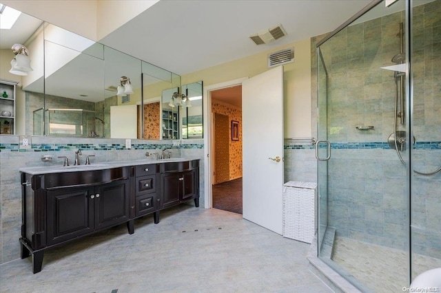 bathroom with a skylight, vanity, a shower with shower door, and tile walls