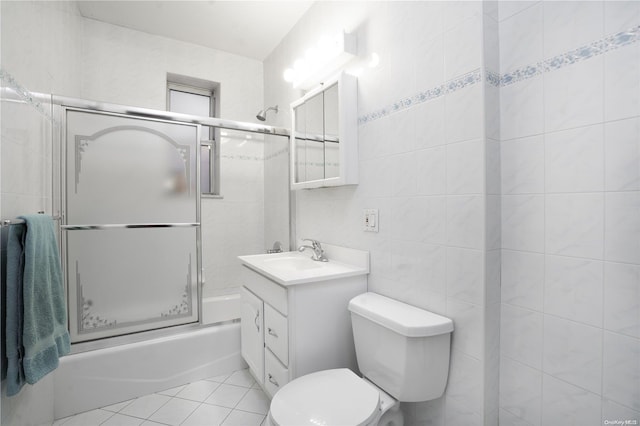 full bathroom with tile patterned flooring, combined bath / shower with glass door, toilet, vanity, and tile walls