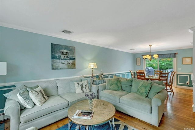 living room with a notable chandelier, light wood-type flooring, and crown molding