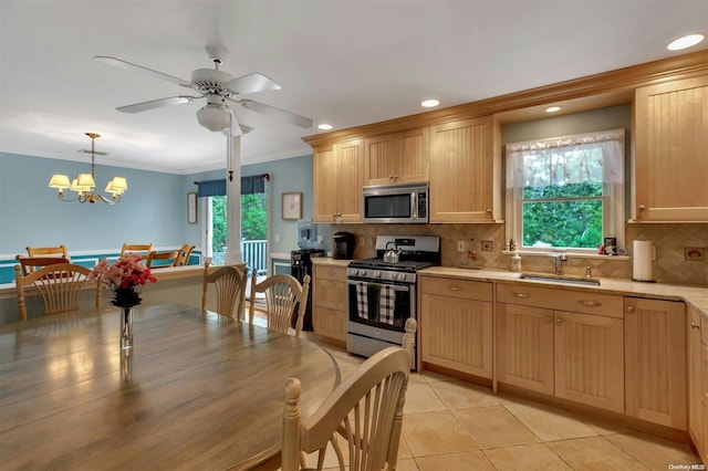 kitchen with light brown cabinets, ceiling fan with notable chandelier, sink, hanging light fixtures, and appliances with stainless steel finishes