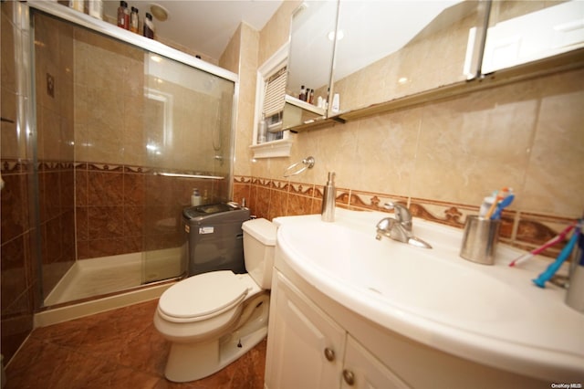 bathroom featuring tile patterned floors, toilet, a shower with door, vanity, and tile walls